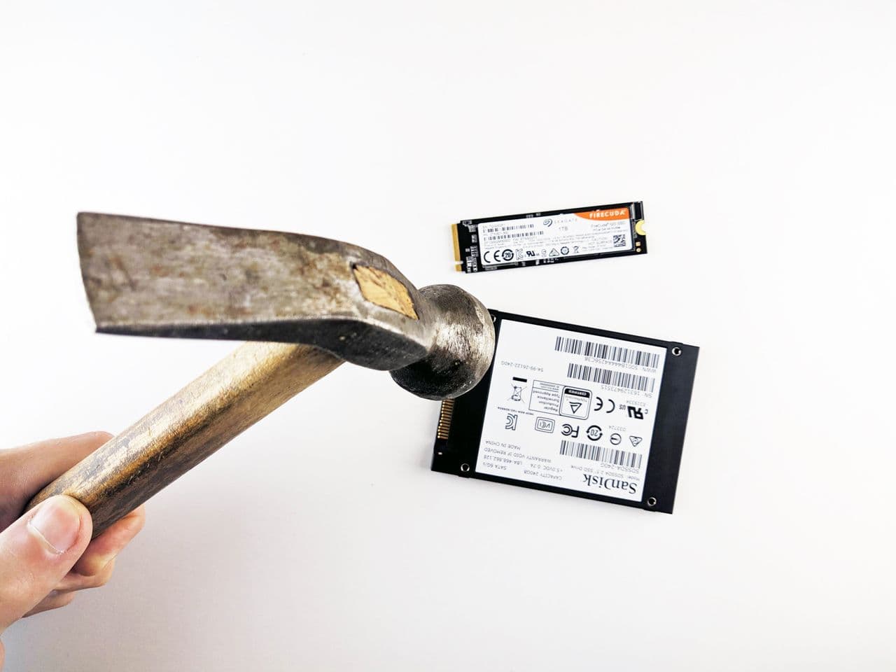 Dłoń z młotkiem tuż nad dyskiem twardym i SSD — symbol fizycznego niszczenia danych